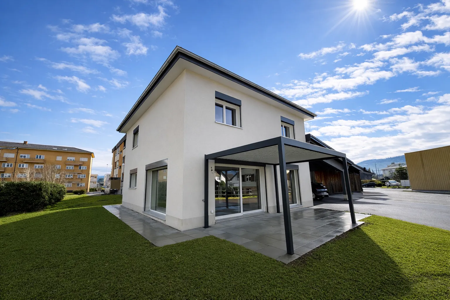 La maison neuve à Courgenay : façade blanche, toit à quatre pans, pergola bioclimatique anthracite sur la terrasse et pelouse.
